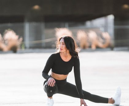 woman in black tank top and black leggings holding black and white nike shoes