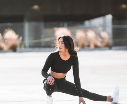 woman in black tank top and black leggings holding black and white nike shoes