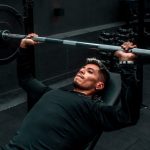 Man performing bench press with heavy barbell in a gym setting, focusing on strength training.
