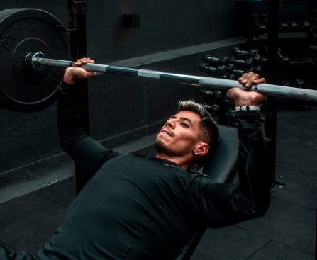 Man performing bench press with heavy barbell in a gym setting, focusing on strength training.