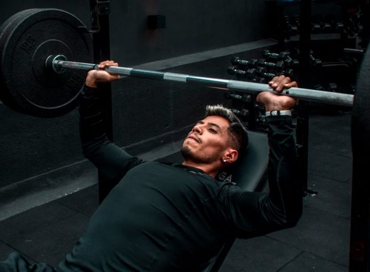 Man performing bench press with heavy barbell in a gym setting, focusing on strength training.